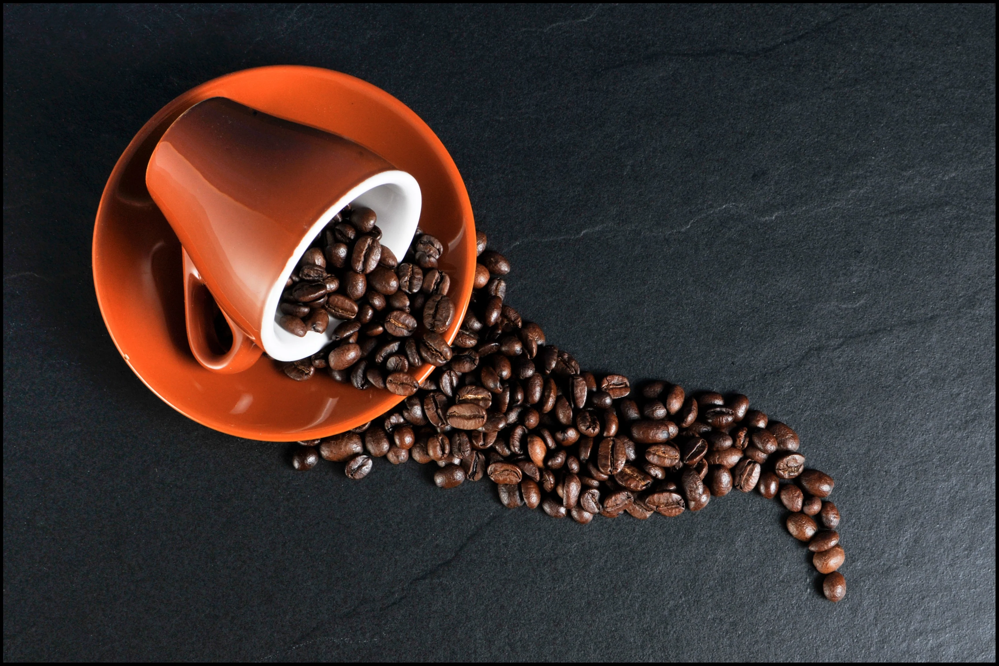 Coffee cup on its slide with beans spread across a surface.