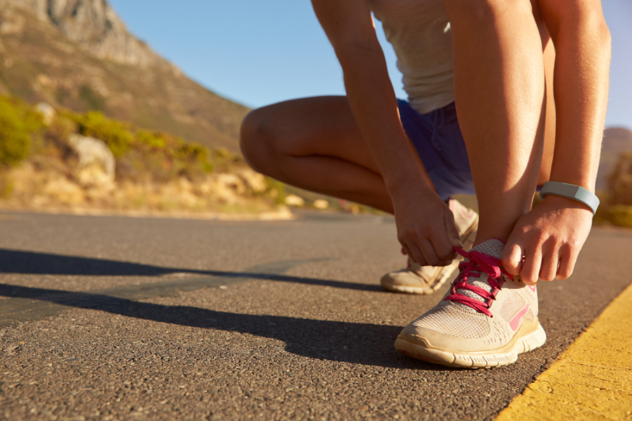 A woman tying her shoelaces on a hot sunny road.