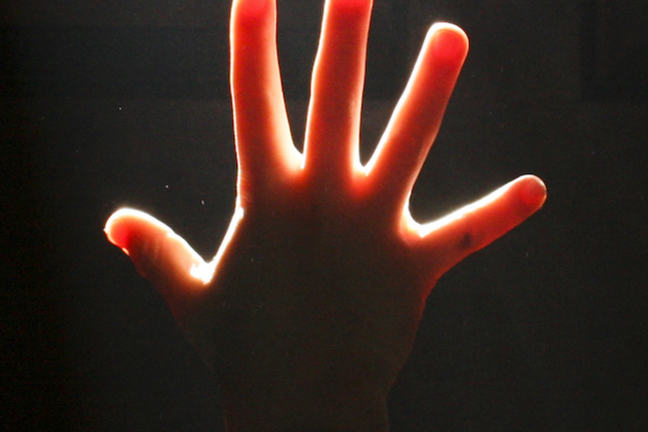A hand illuminated against a dark background showing five fingers