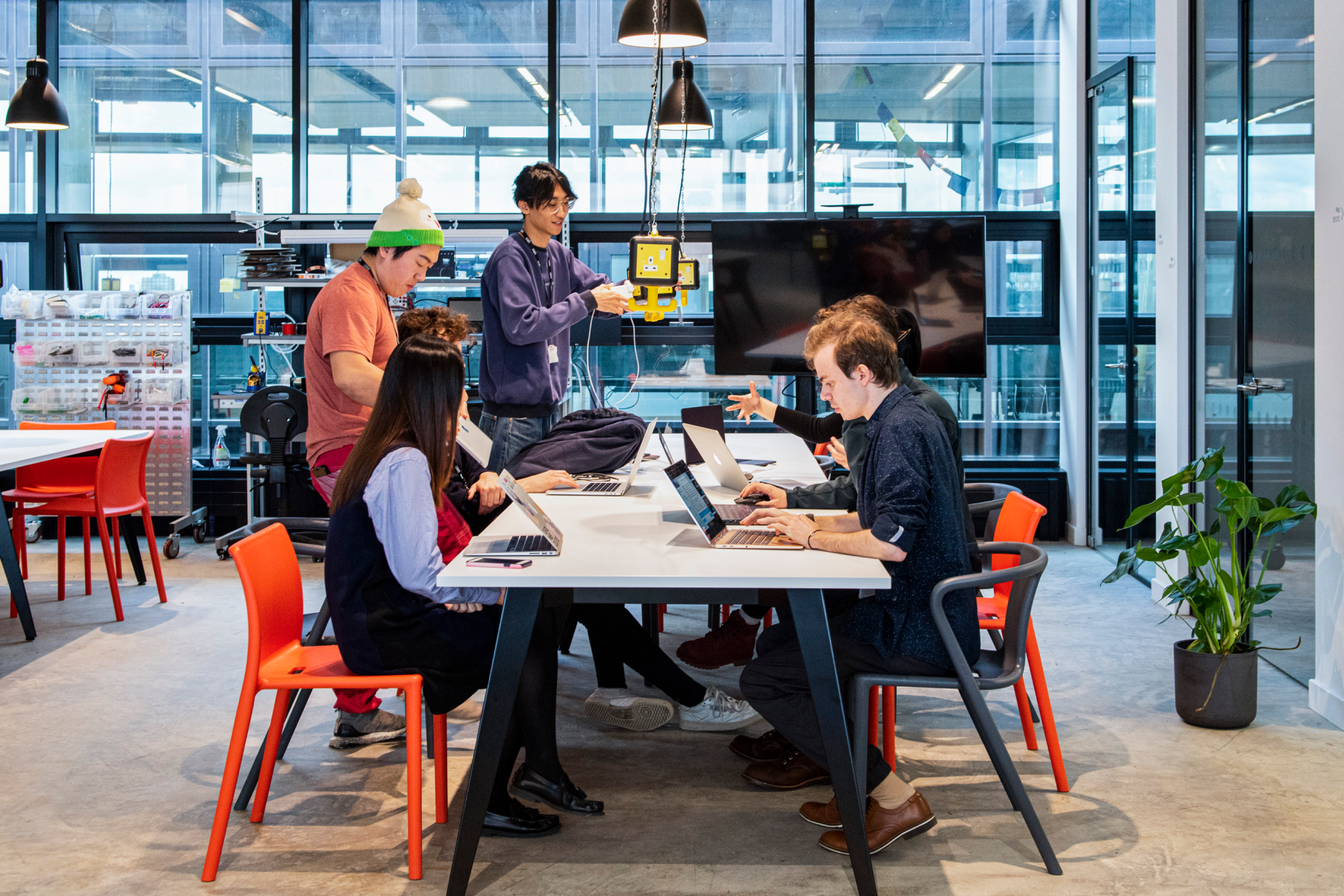 an image of a team of people sat around a table. Some are on their laptops, some are taking notes.