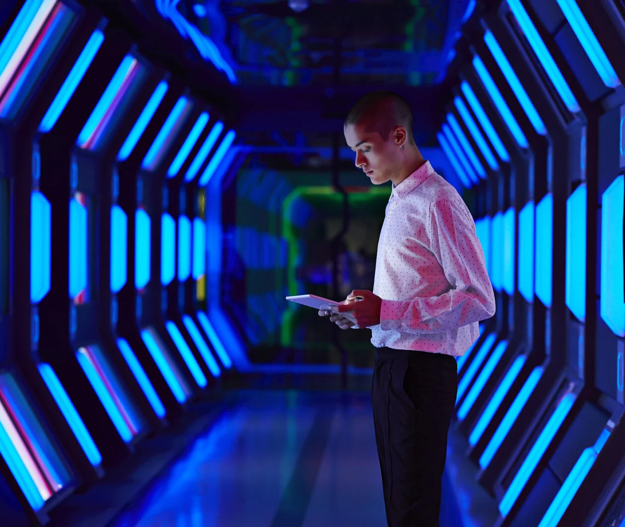 a young man standing with a tablet inside a data warehouse with futuristic lighting