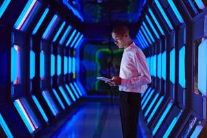 a young man standing with a tablet inside a data warehouse with futuristic lighting