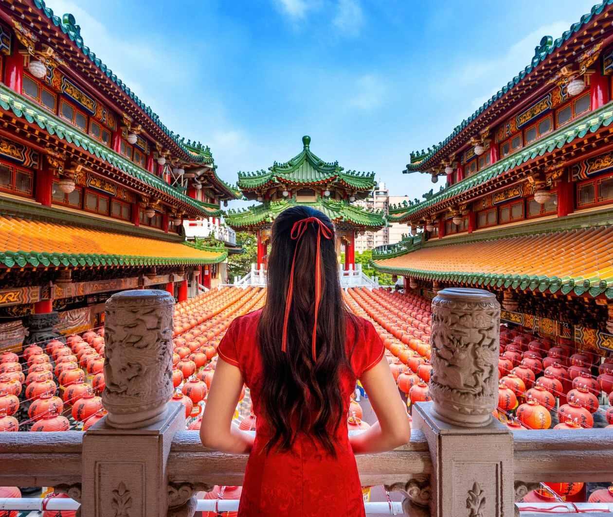 Chinese woman standing with her back to the camera facing a temple filled with rows of traditional Chinese lanterns.