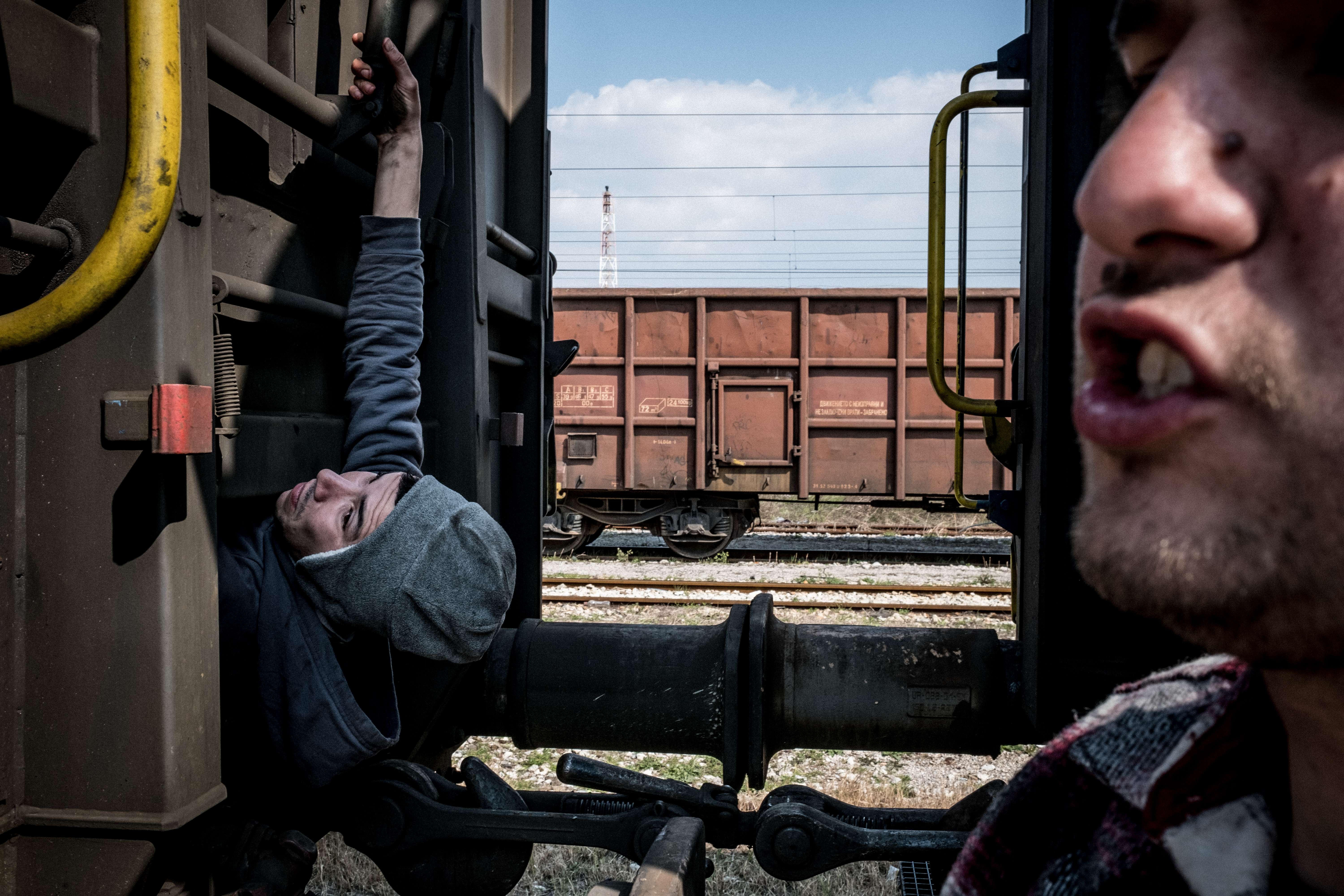 Two unaccompanied teenage boys are hanging from a moving train, trying to find a way to hold on and hide to allow them to cross borders.