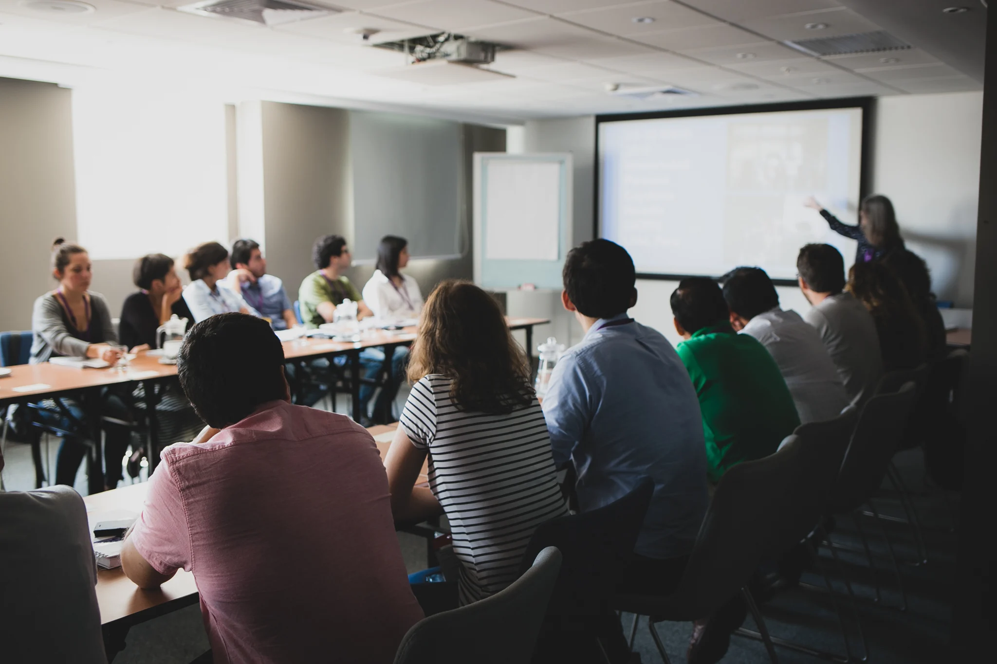 Teacher standing in front of a white board with group of students seated on two sides facing each others,  listening