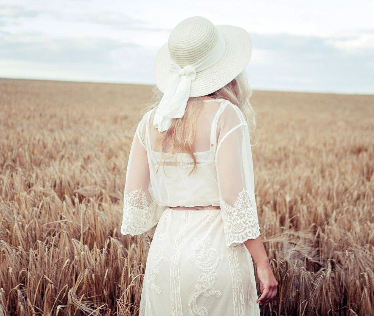 A young woman in a white sheer dress and white hat exploring a field of wheat