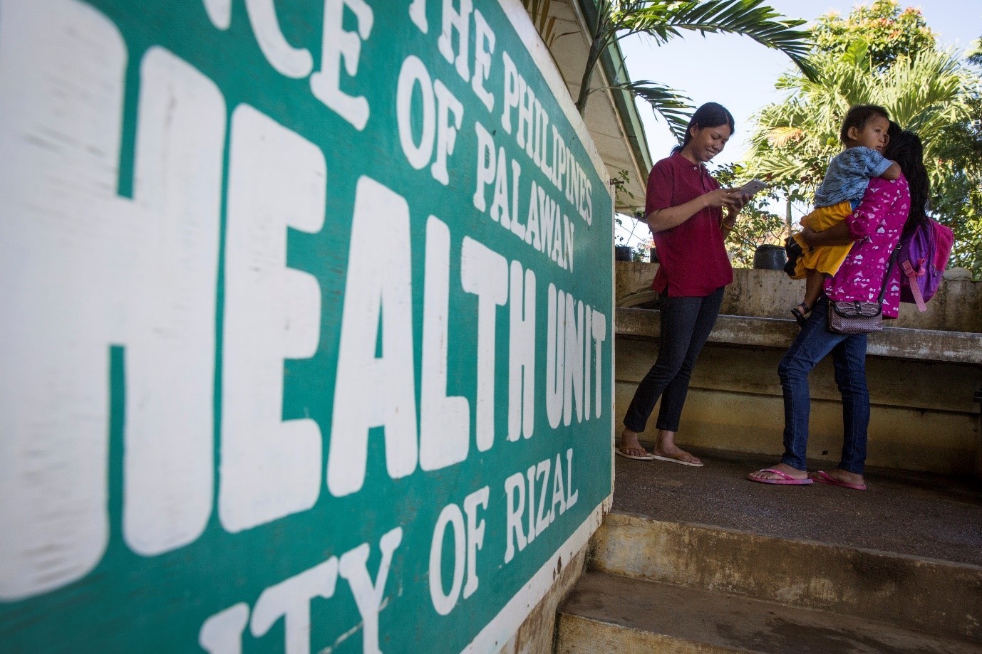 Two mothers and a child stand outside of a health unit in the Philippines