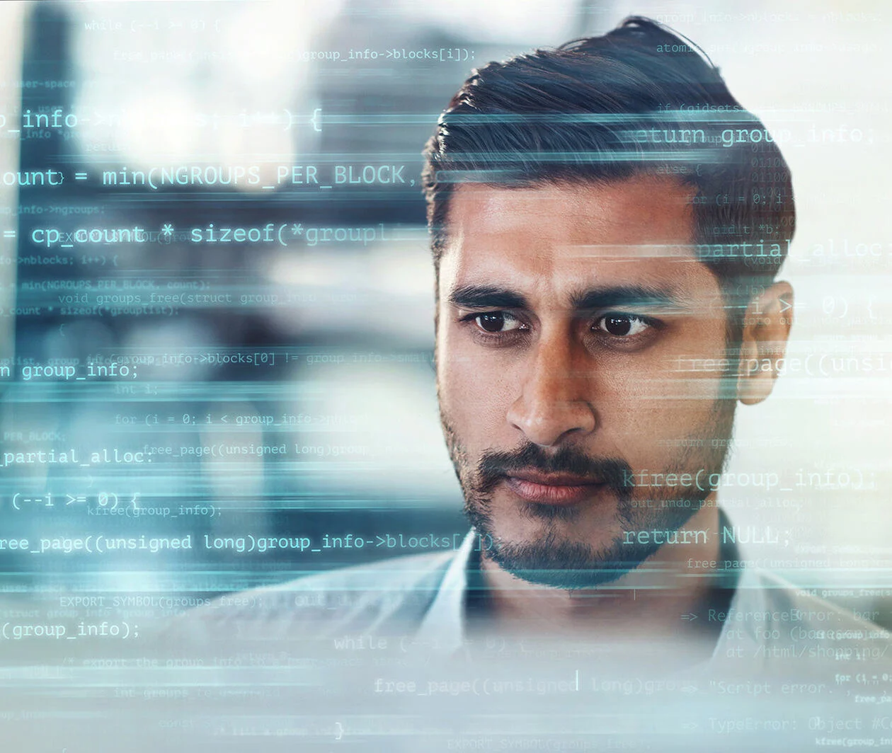 A man in a shirt sits on a computer in an office setting with code surrounding him.