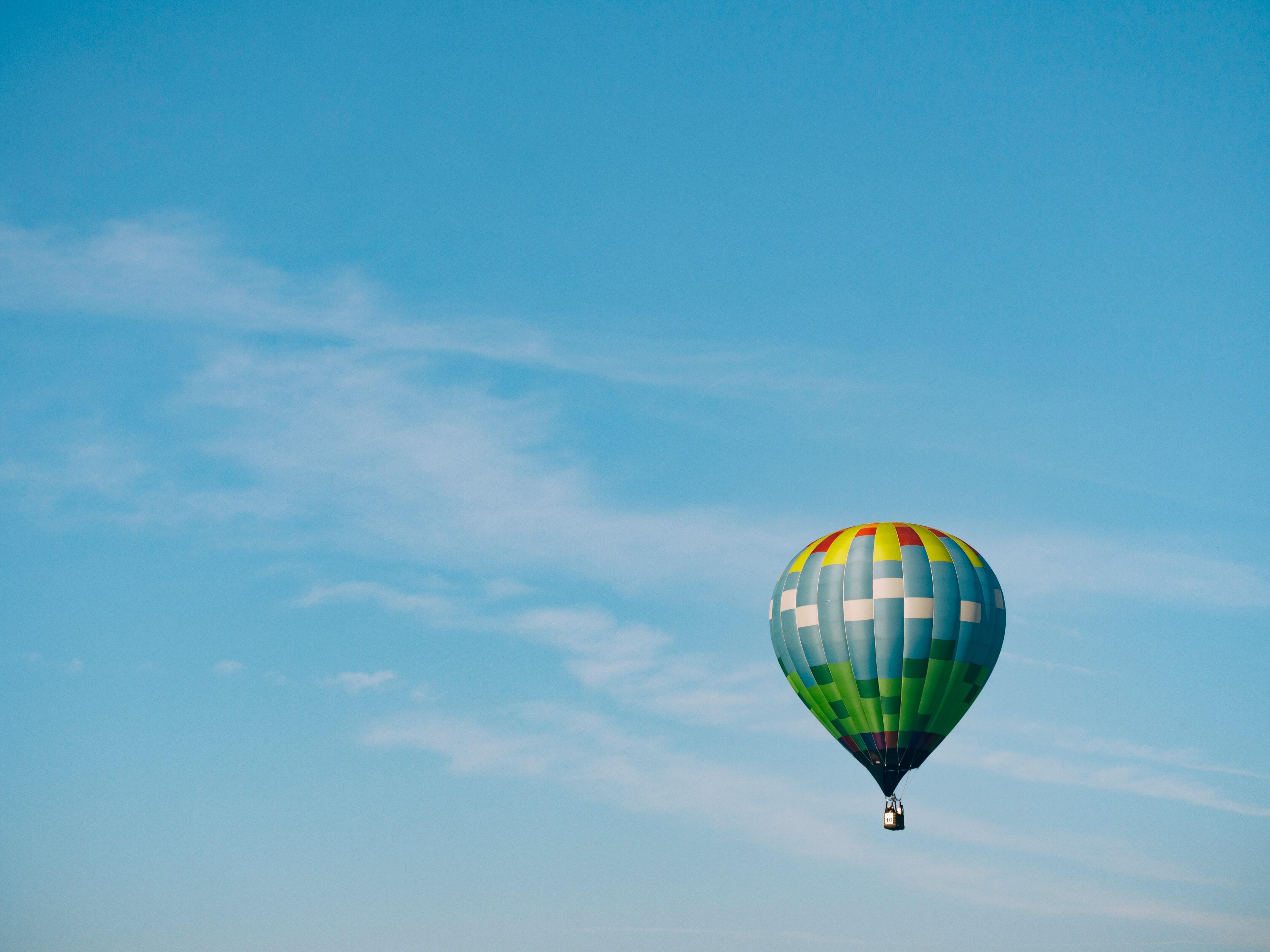 A photograph of a colourful air balloon floating against a cloudless blue sky by Aaron Burden.