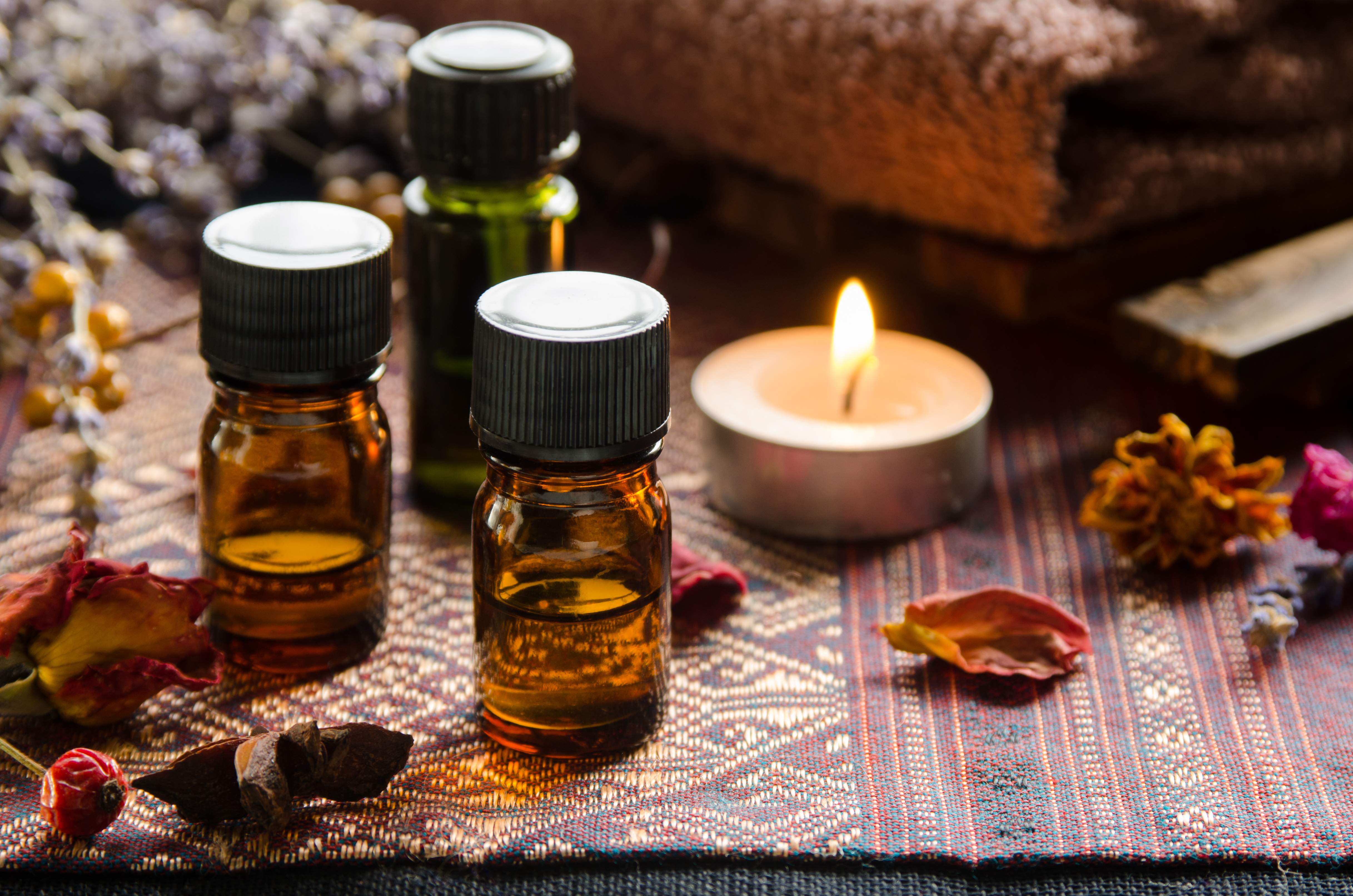 Small jars of bath oil next to flowers and a candle