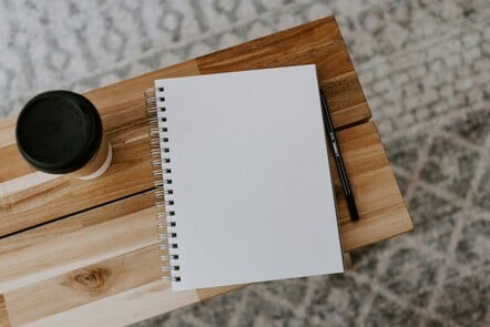 A blank notebook with a pen beside it laying flat on a table.