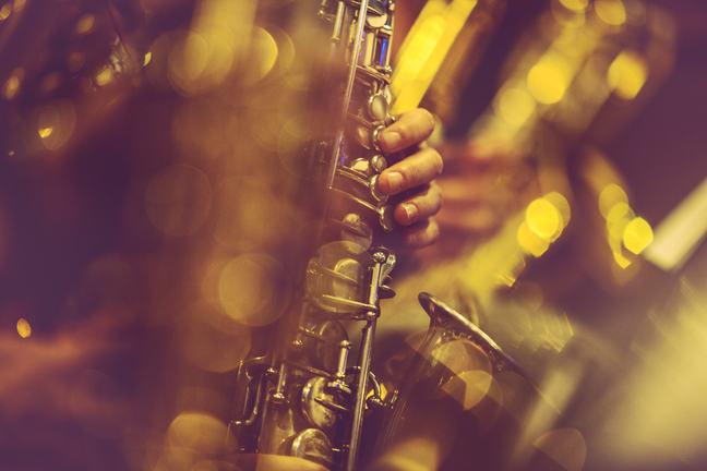 Uma foto de um saxofone, com um close-up na mão do saxofonista.