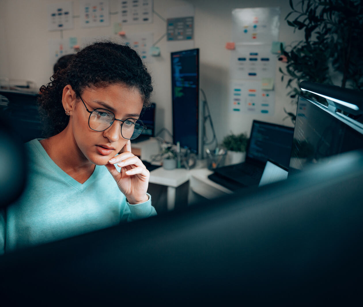 Young woman sits at a computer with her hand on her chin