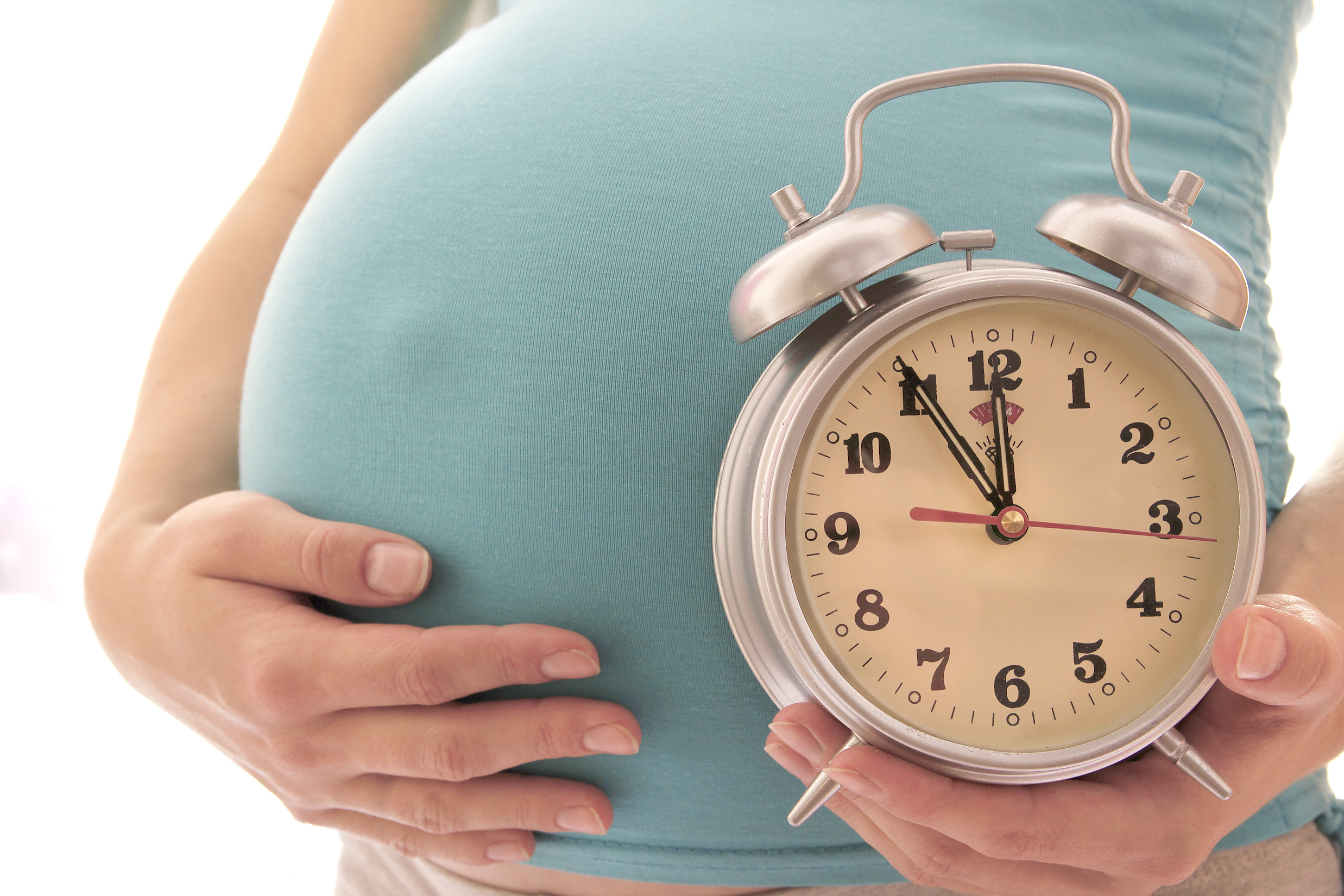 A woman cradles her baby bump while holding an old fashioned alarm clock