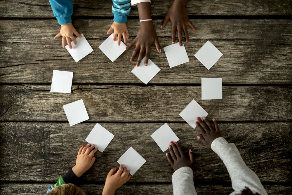 Four childrens' hands forming a love heart with white cards