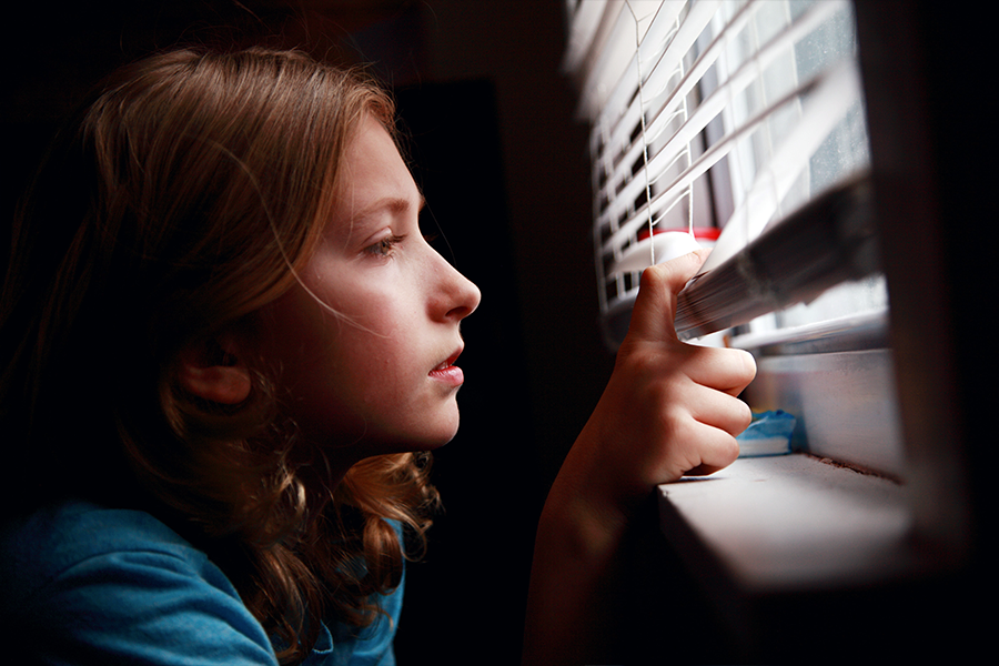 Young girl looking nervously through blinds