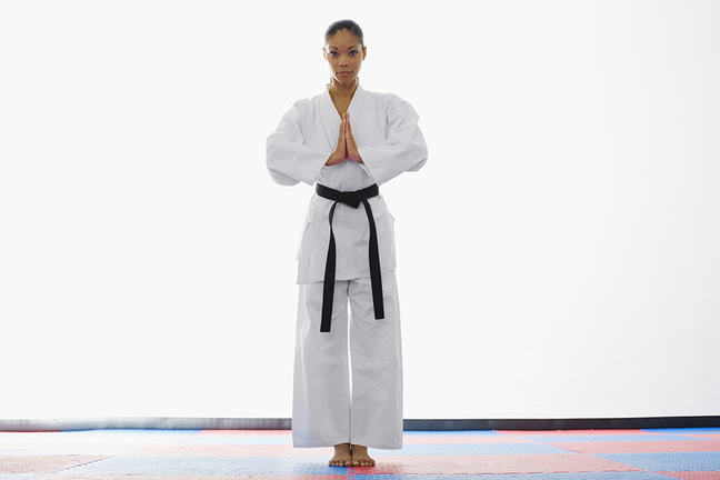 woman in white martial arts clothing with a black belt standing.