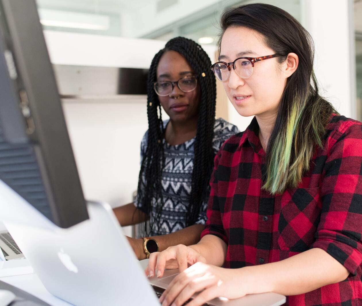 Two women working on their English sentence structure, punctuation, and written communication at a computer