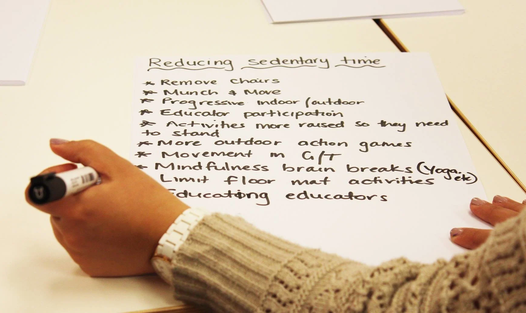 photograph of a person writing a list of strategies for reducing sedentary time and creating active spaces for children (e.g. remove chairs, munch and move, education, yoga etc.)