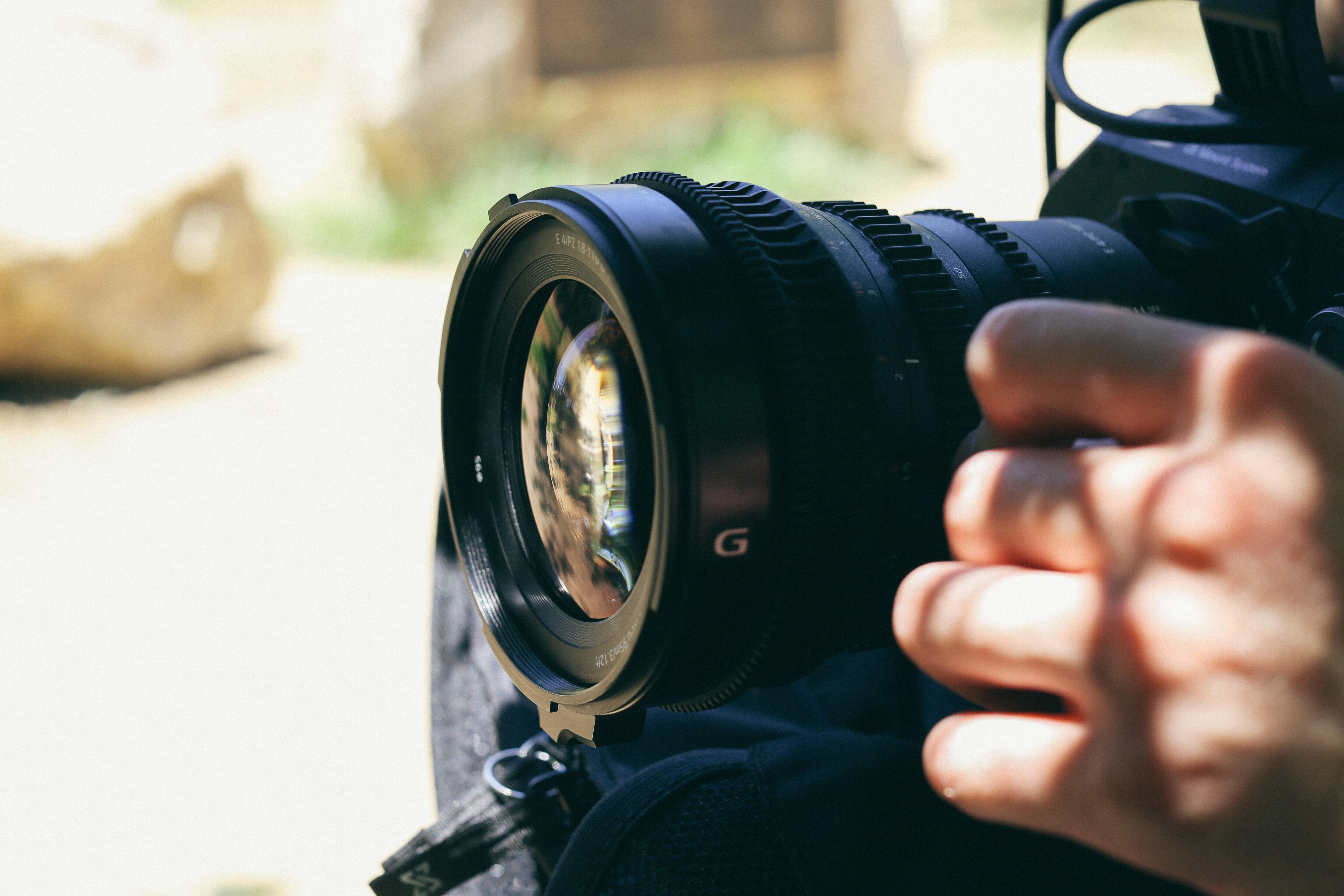 Close-up of hands holding a black DSLR camera outdoors.