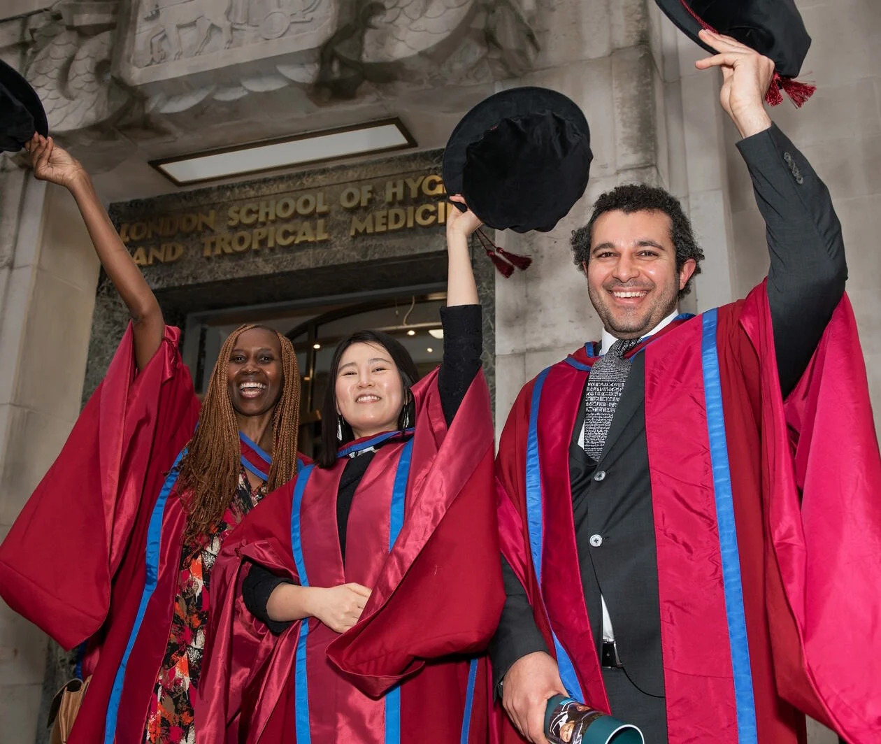 A group of three doctoral graduates in regalia and waving their bonnets.