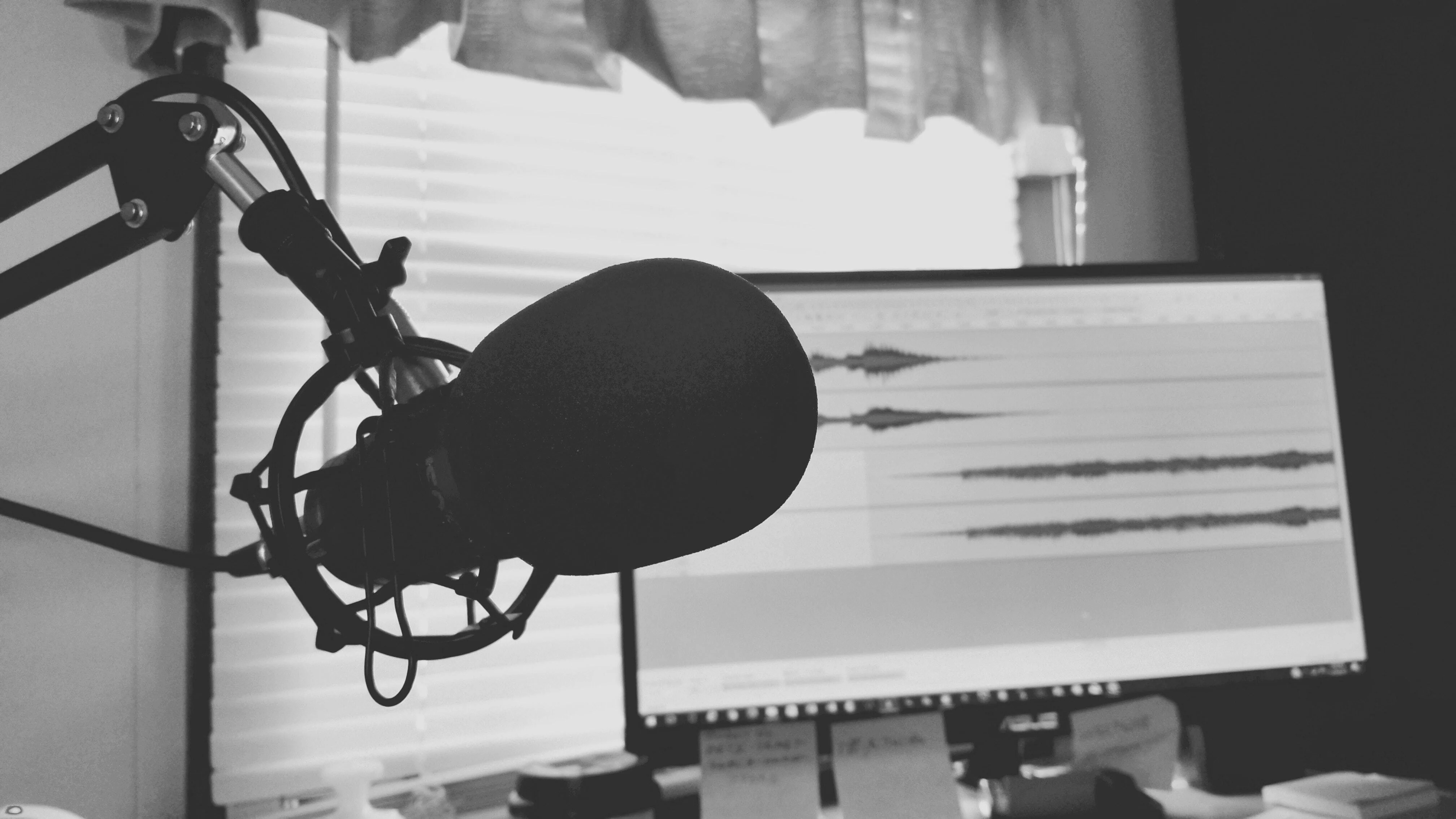 Black and white image of a podcast set with a microphone and a screen with audio recordings