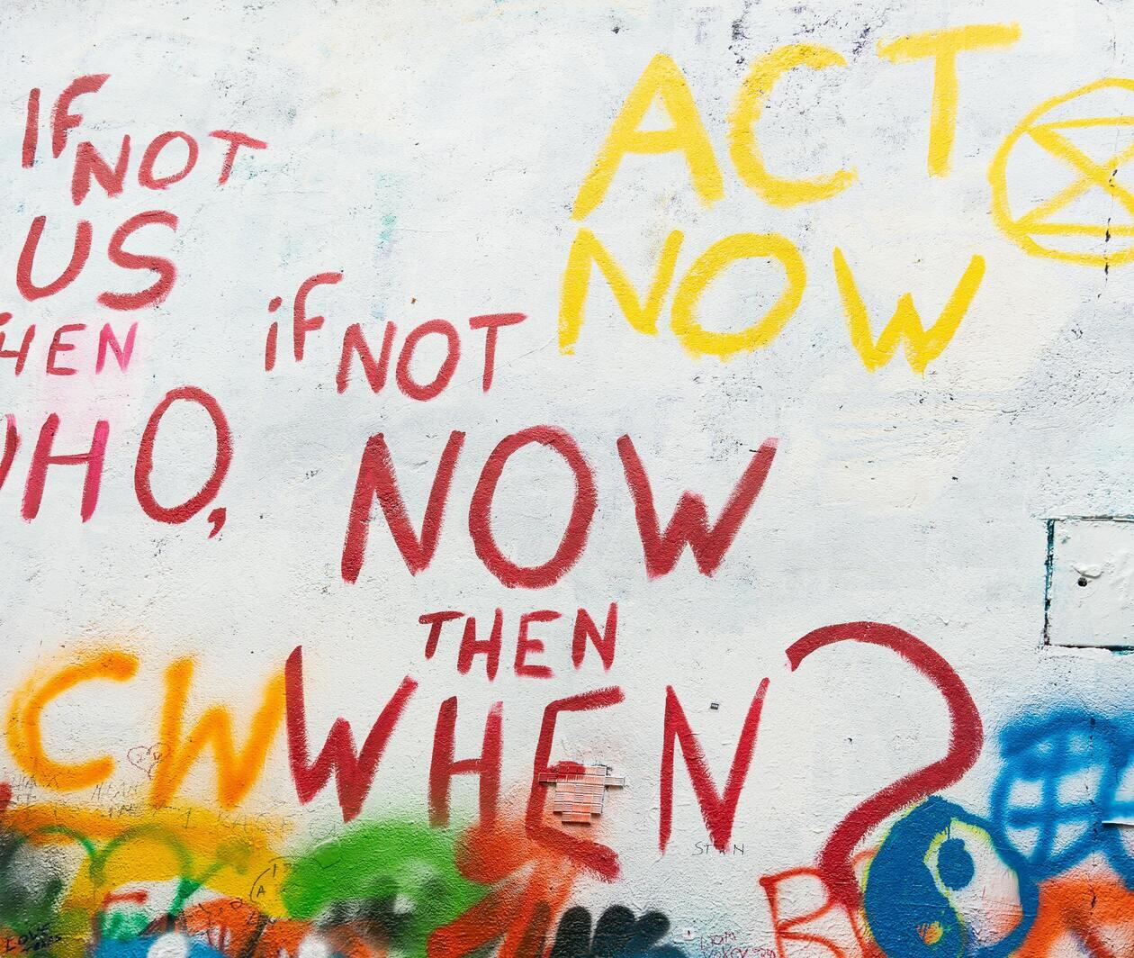 Photo by Rod Long on Unsplash of red graffiti on a white wall reading "If not us, then who? If not now, then when?" and yellow graffiti reading "Act now"