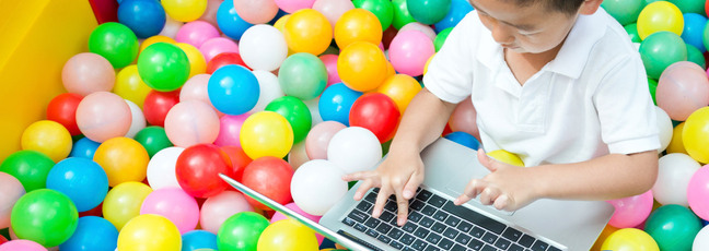 A child using a laptop in a colourful ball pool