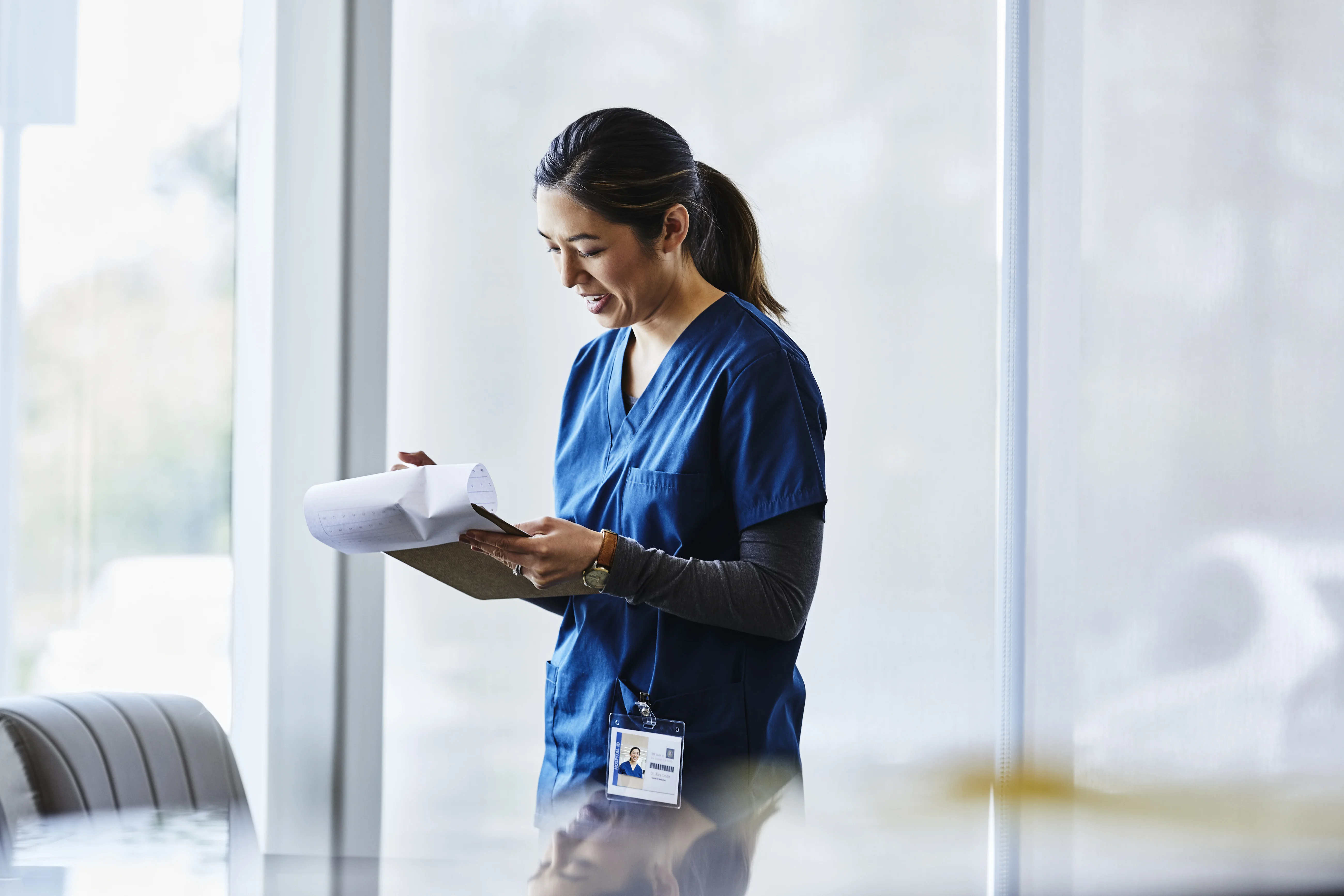 Smiling female nurse examining document in hospital lobby.