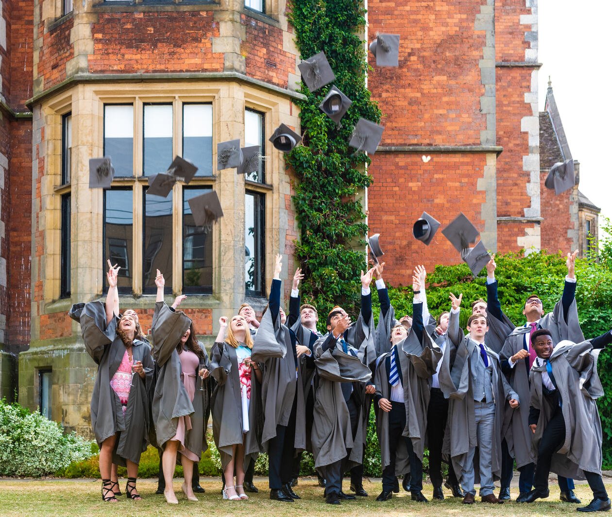 Students from the University of York standing outside a red-brick university building and throwing their mortarboard hats.