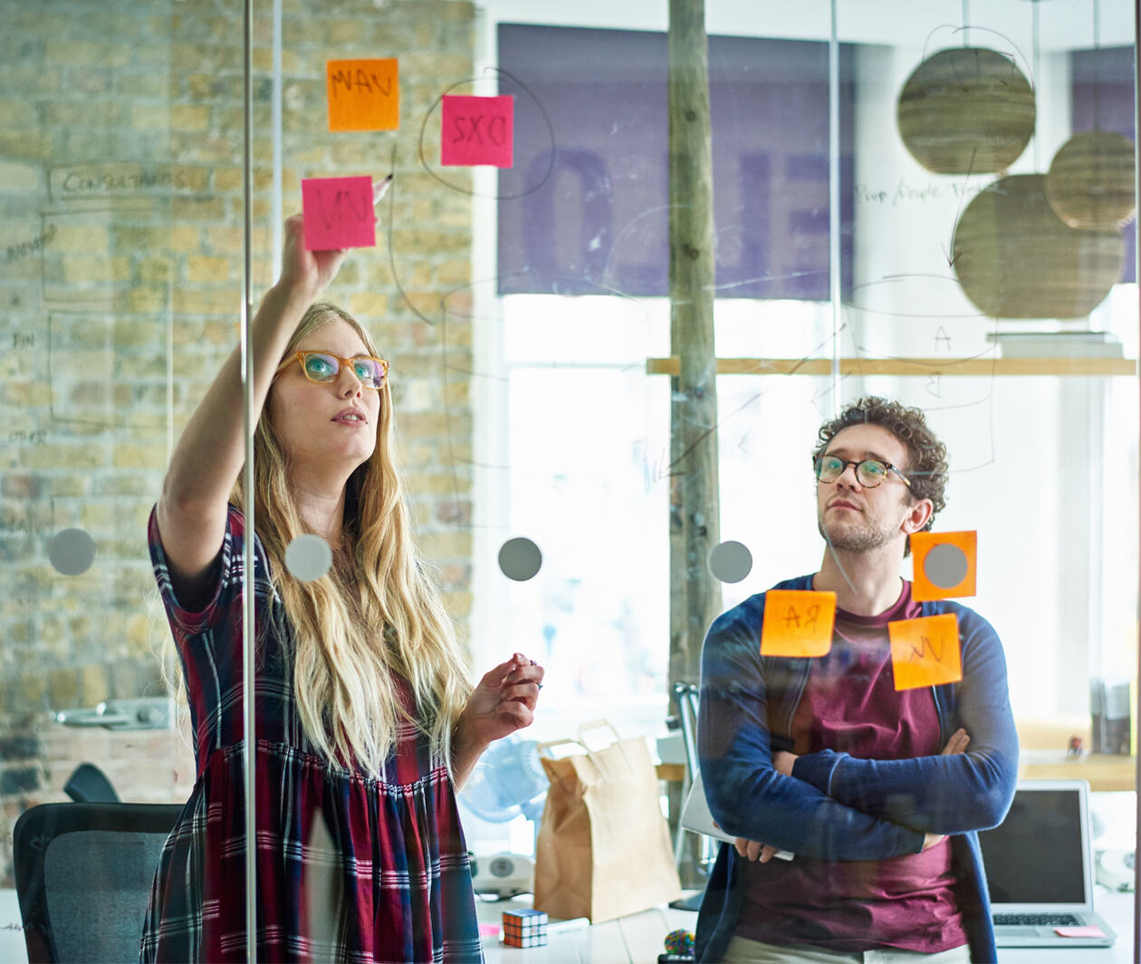 Businesswoman and businessman drawing on glass in modern office, working on a project planning and management together.