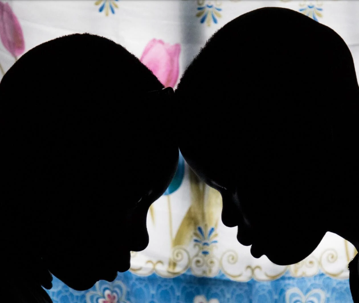 Silhouettes of two young boys facing each other in front of a colourful piece of cloth