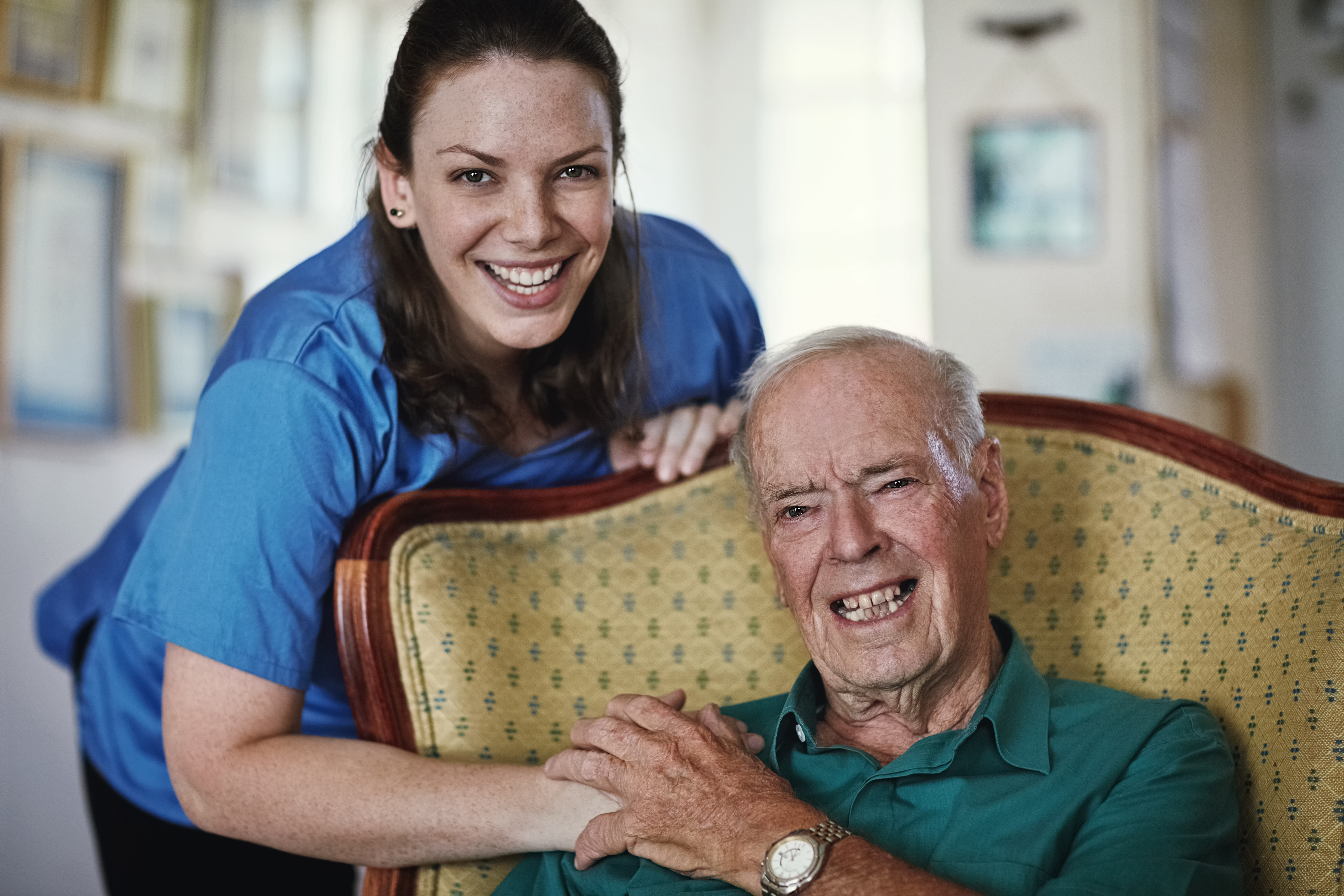 Female social care worker hugging older man sitting in his chair