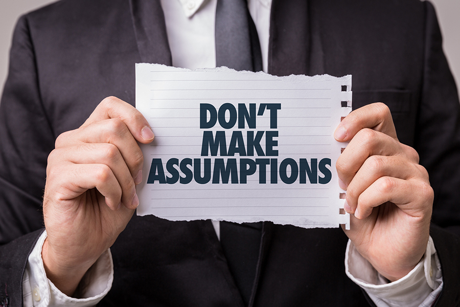 Business person holding a paper note saying 'Don't make assumptions'.