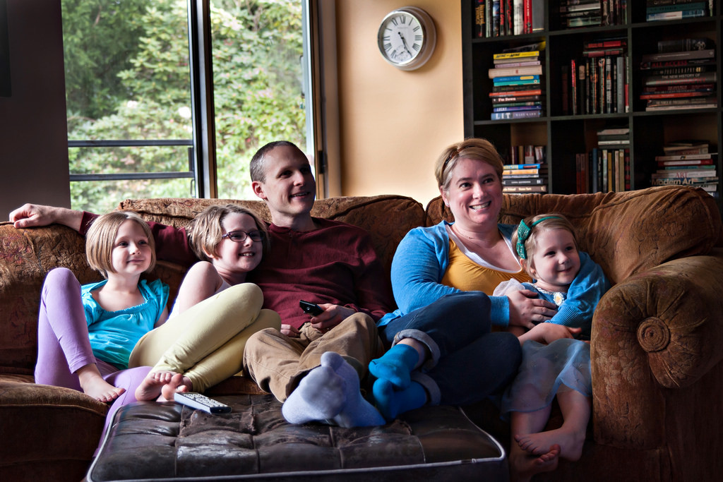 Family of 5 sitting on lounge smiling and watching television