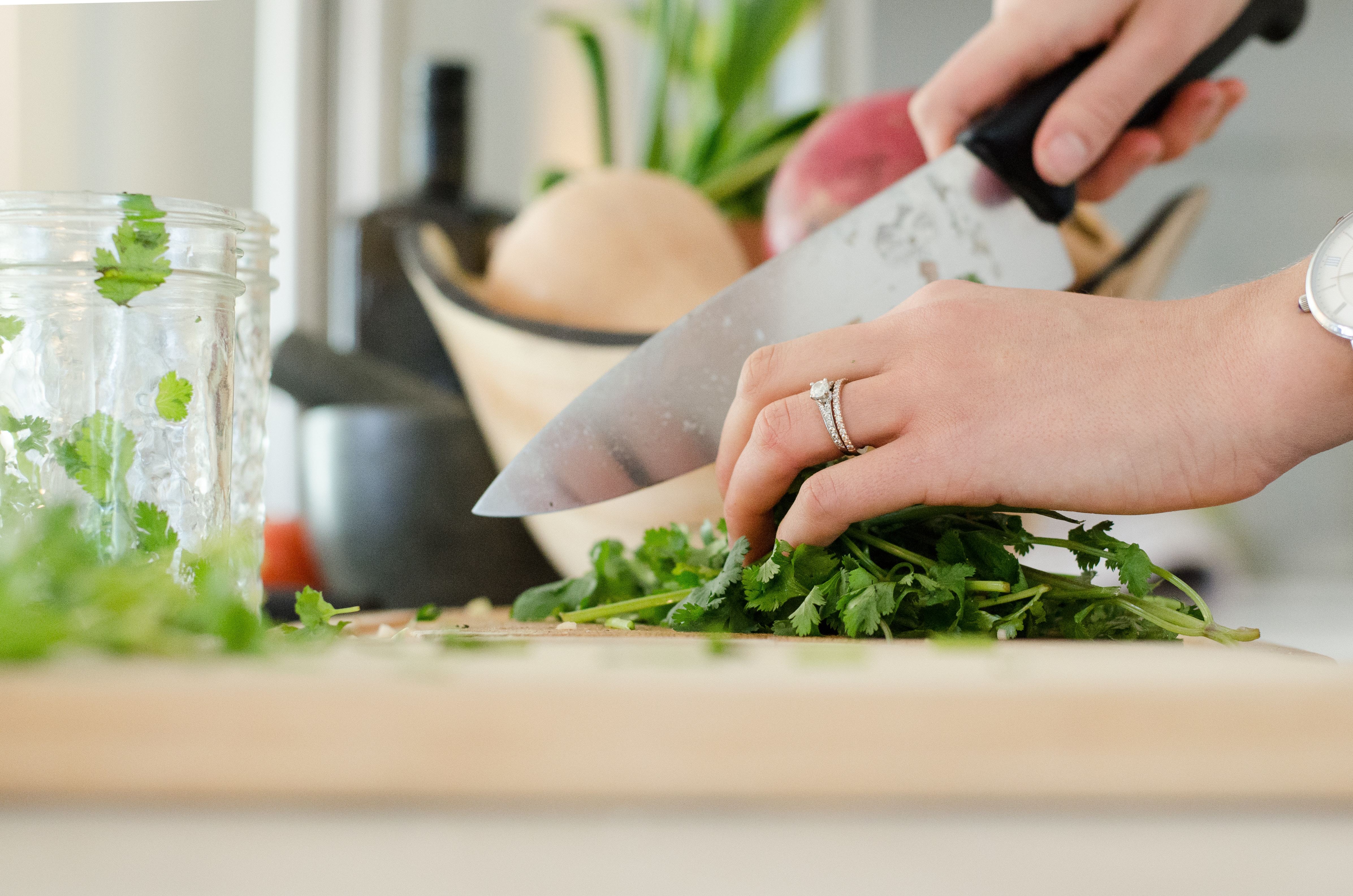 A close-up of a hand holding a kitchen knife and chopping herbs