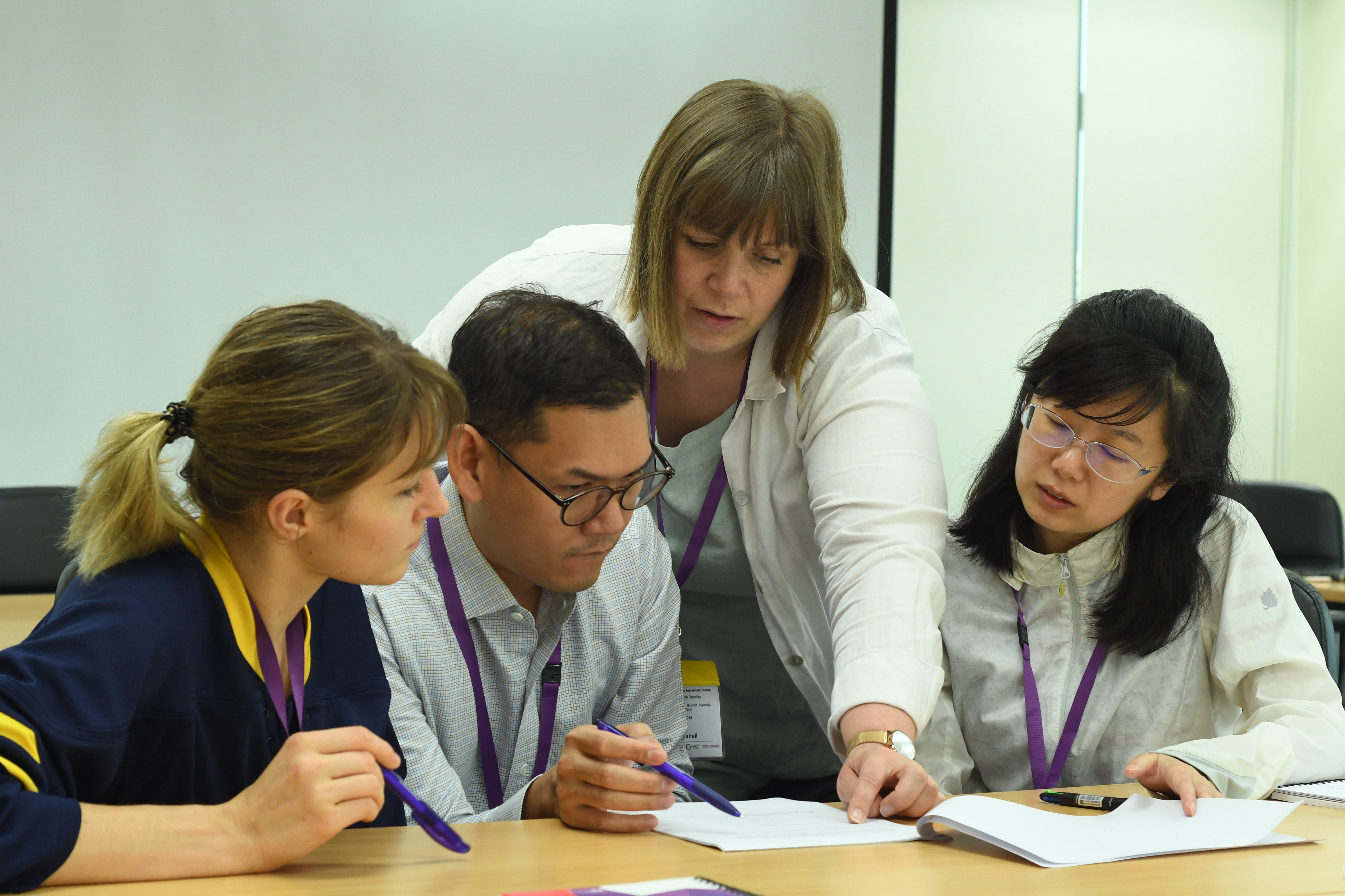 three learners sitting at a desk and concentrating on some work, with a trainer helping/explaining