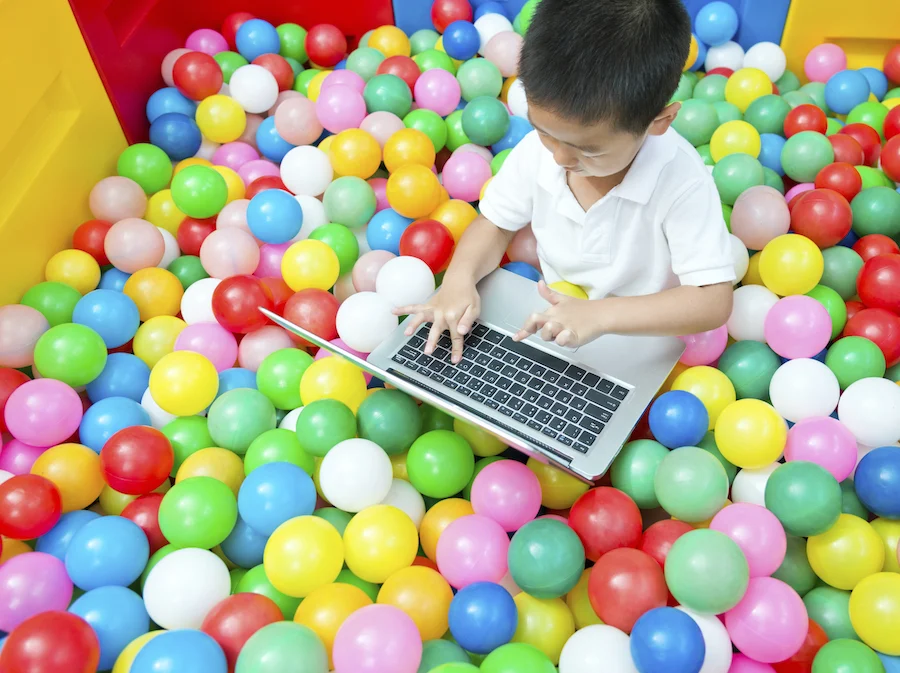 a younger student on a laptop in a ball pool