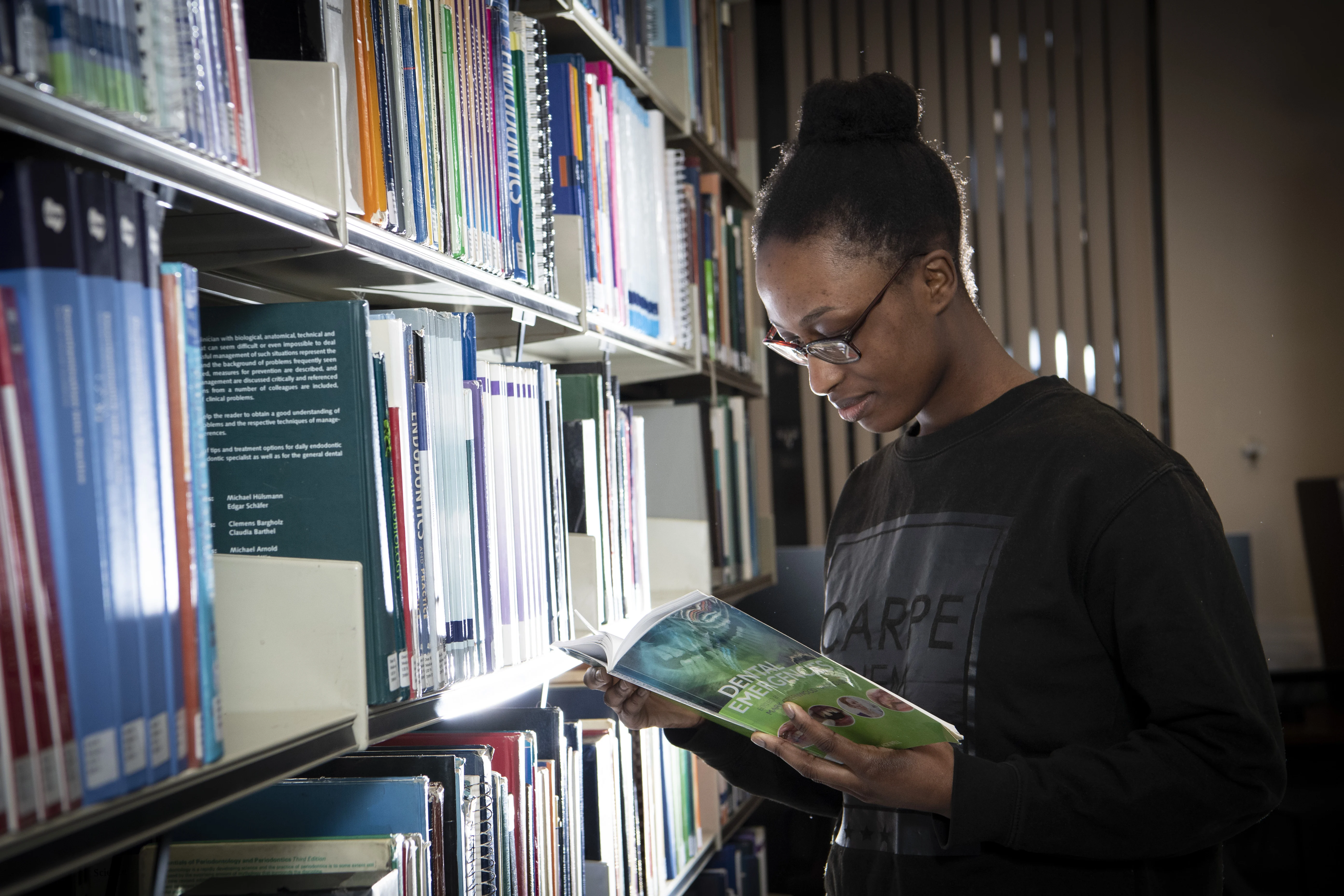 Photograph of a female student in a library reading a book