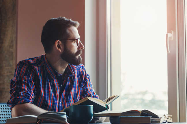 Man thinking while looking out of window and holding a book