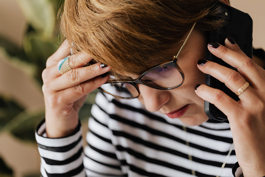 A woman on the phone rests her head in her hand and looks deep in thought.