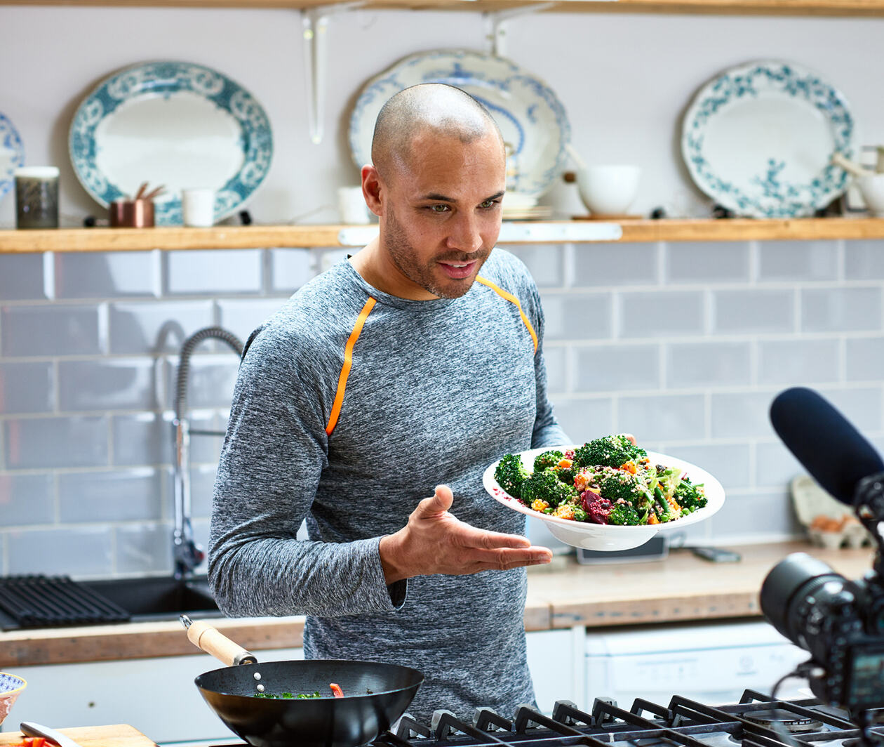 A man in a kitchen talking to camera with a plate of healthy food