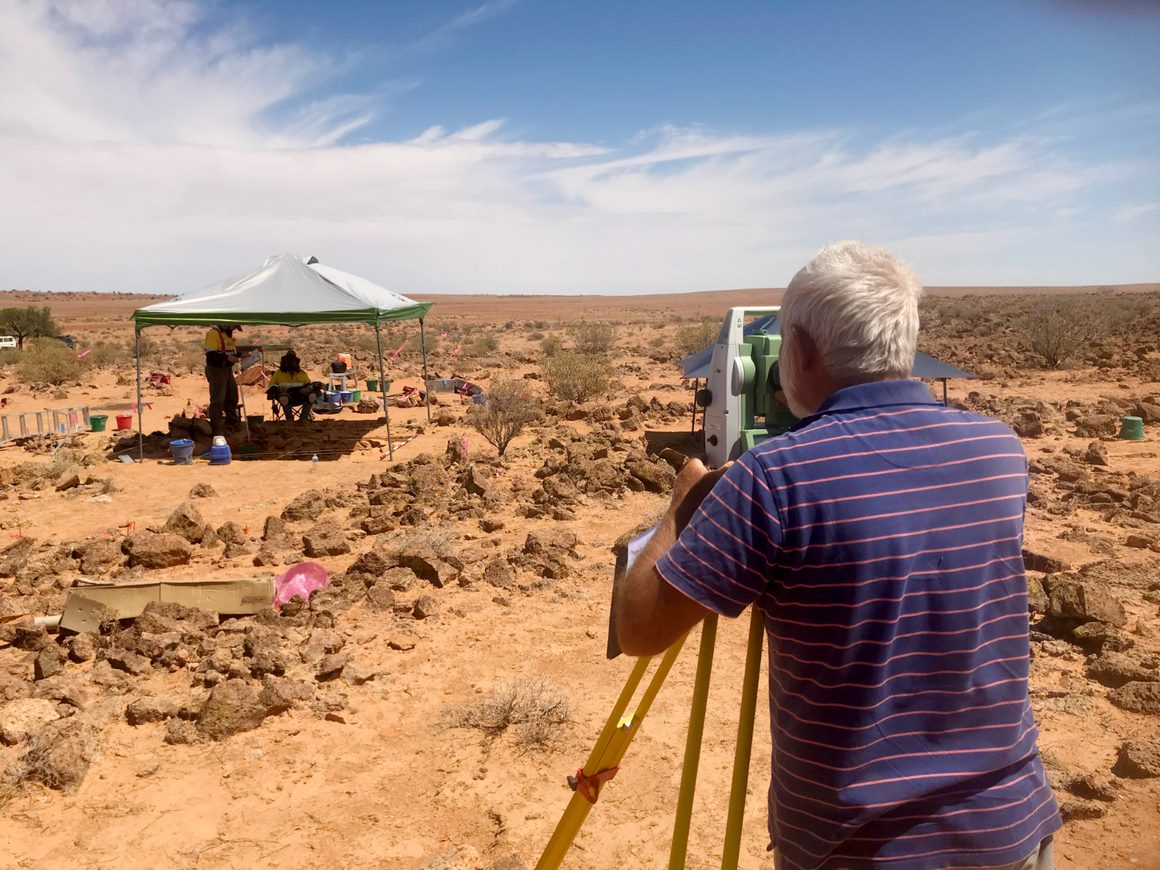 Ian Andrews surveying an archaeological while other researchers document the finds under a tent