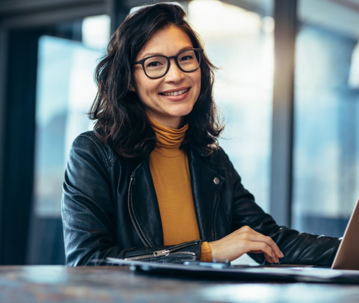 A woman using laptop computer on a desk smiling and looking into the camera