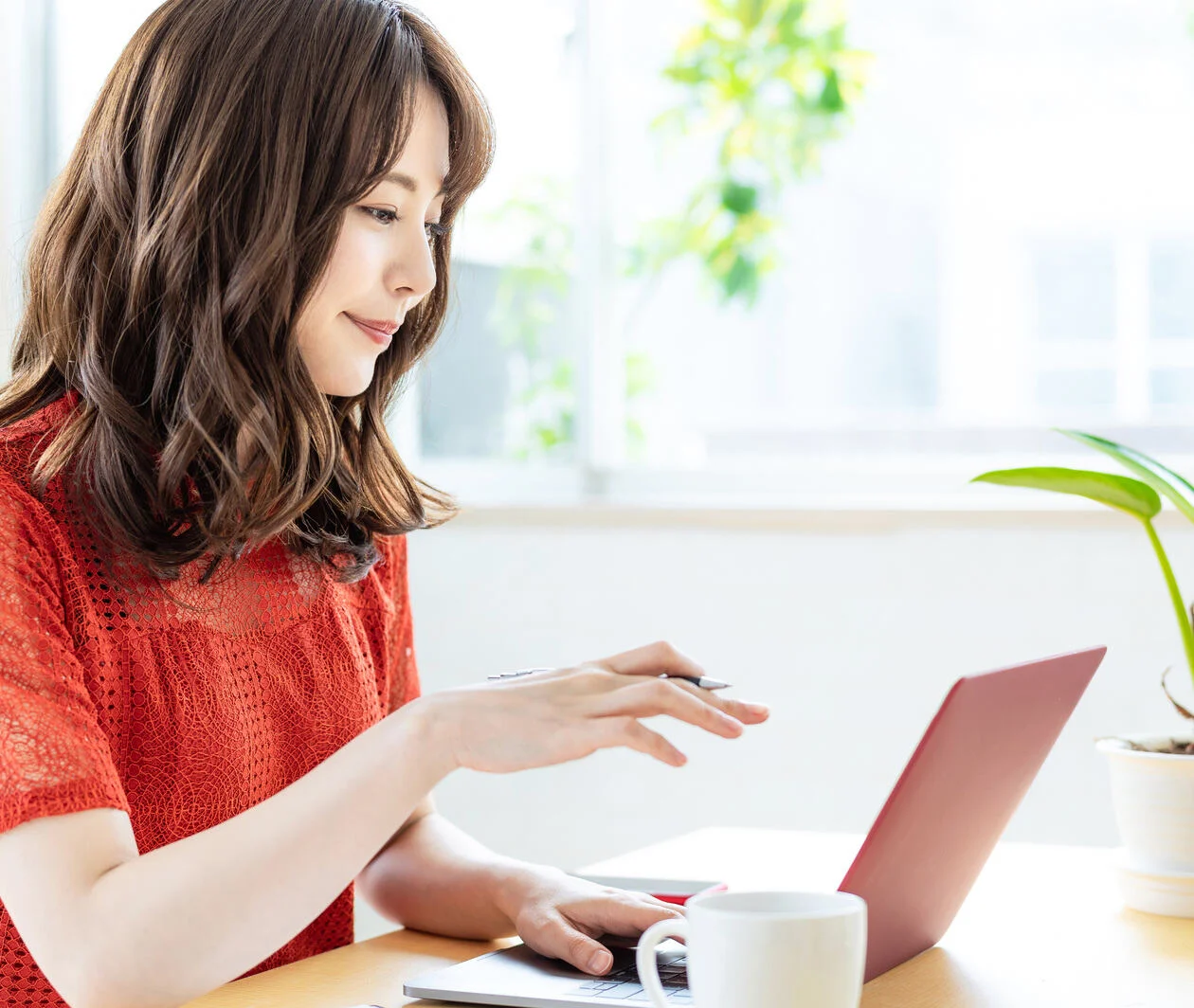 A young asian woman sitting in a park gazing into the distance. Laptop in front of her, taking a break from work.