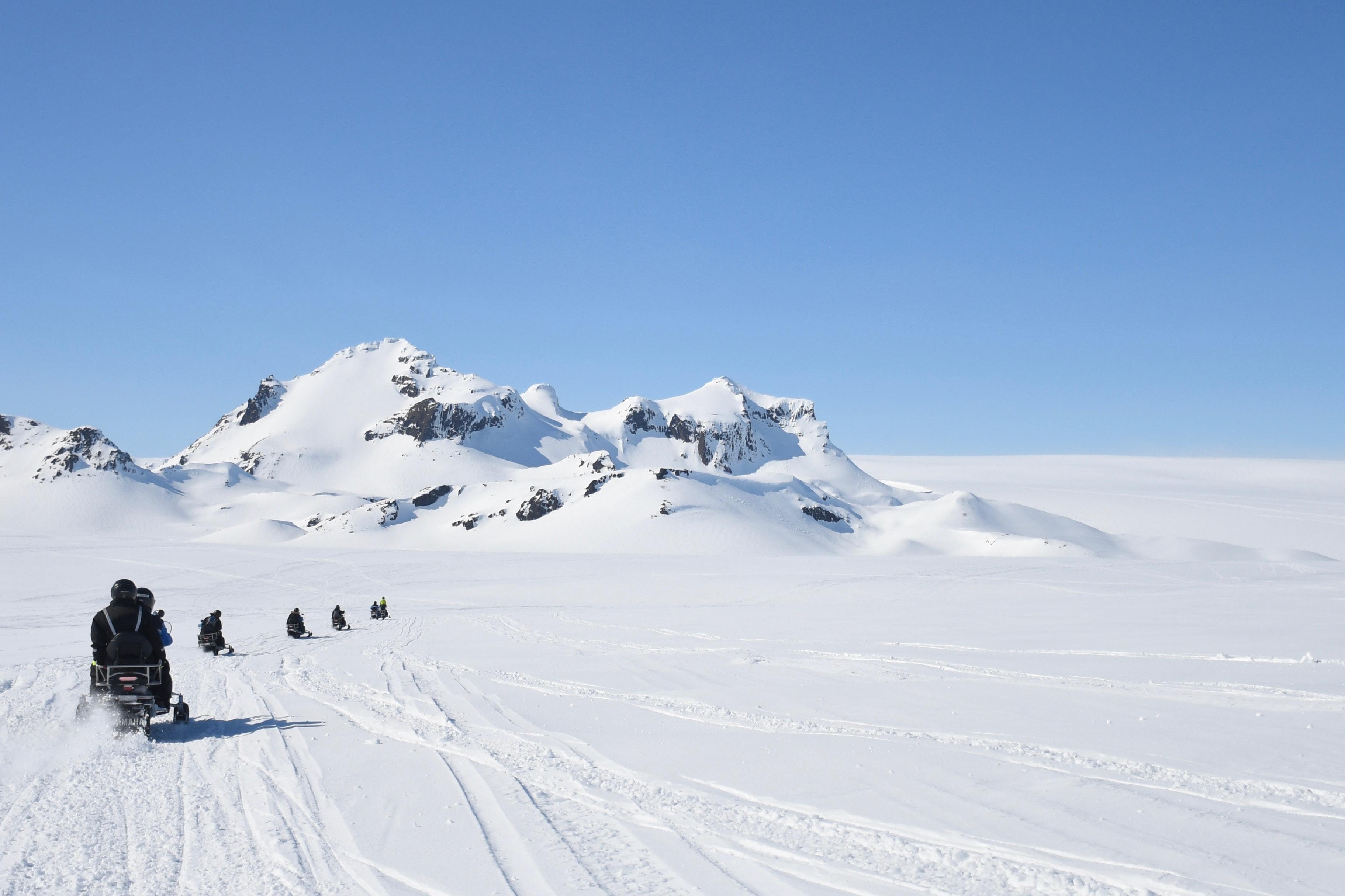 Image of a team of scientists snowmobiling across a snowy landscape