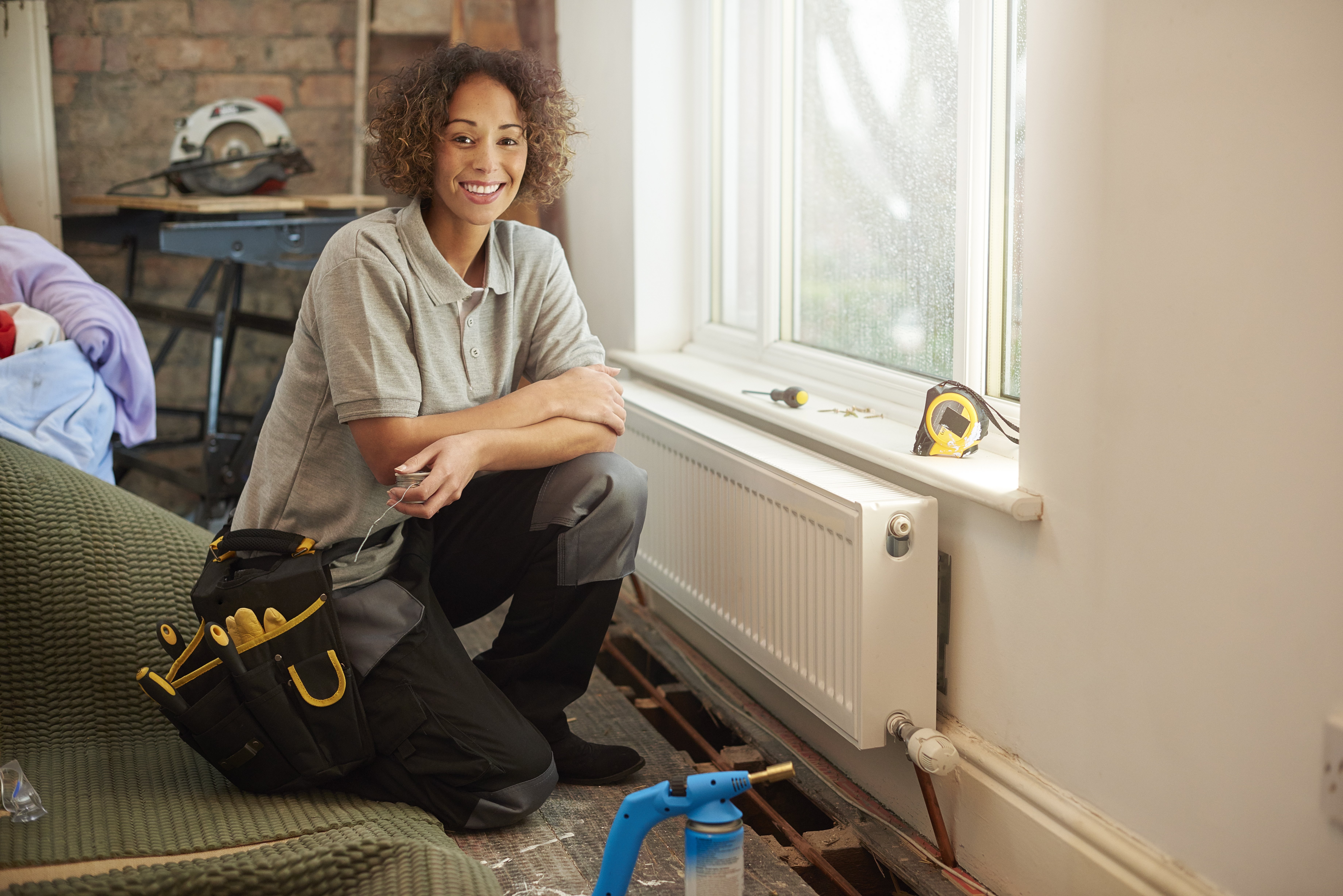 Woman heating engineer kneeling next to radiator