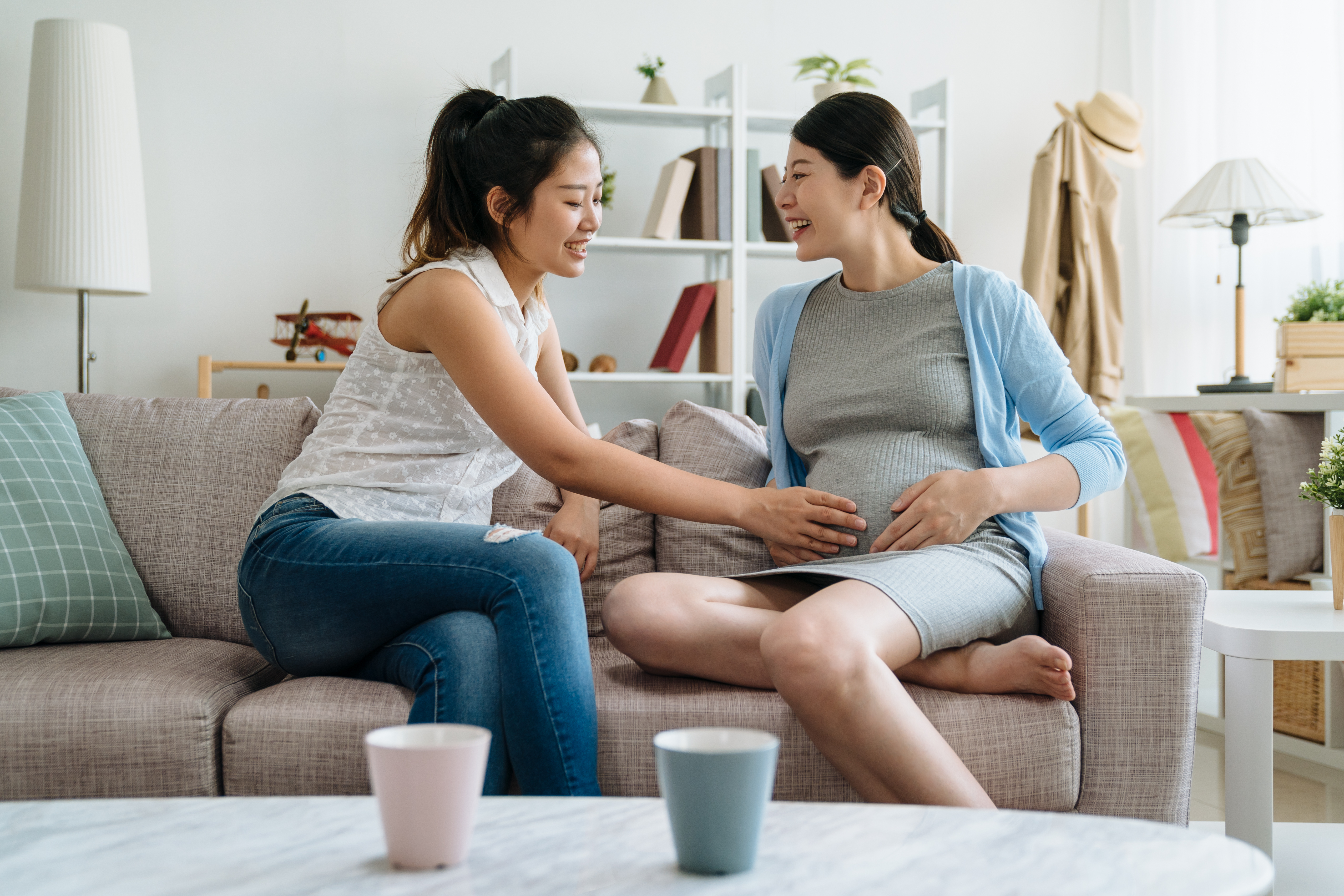 A friend placing a hand on a pregnant woman's baby bump.