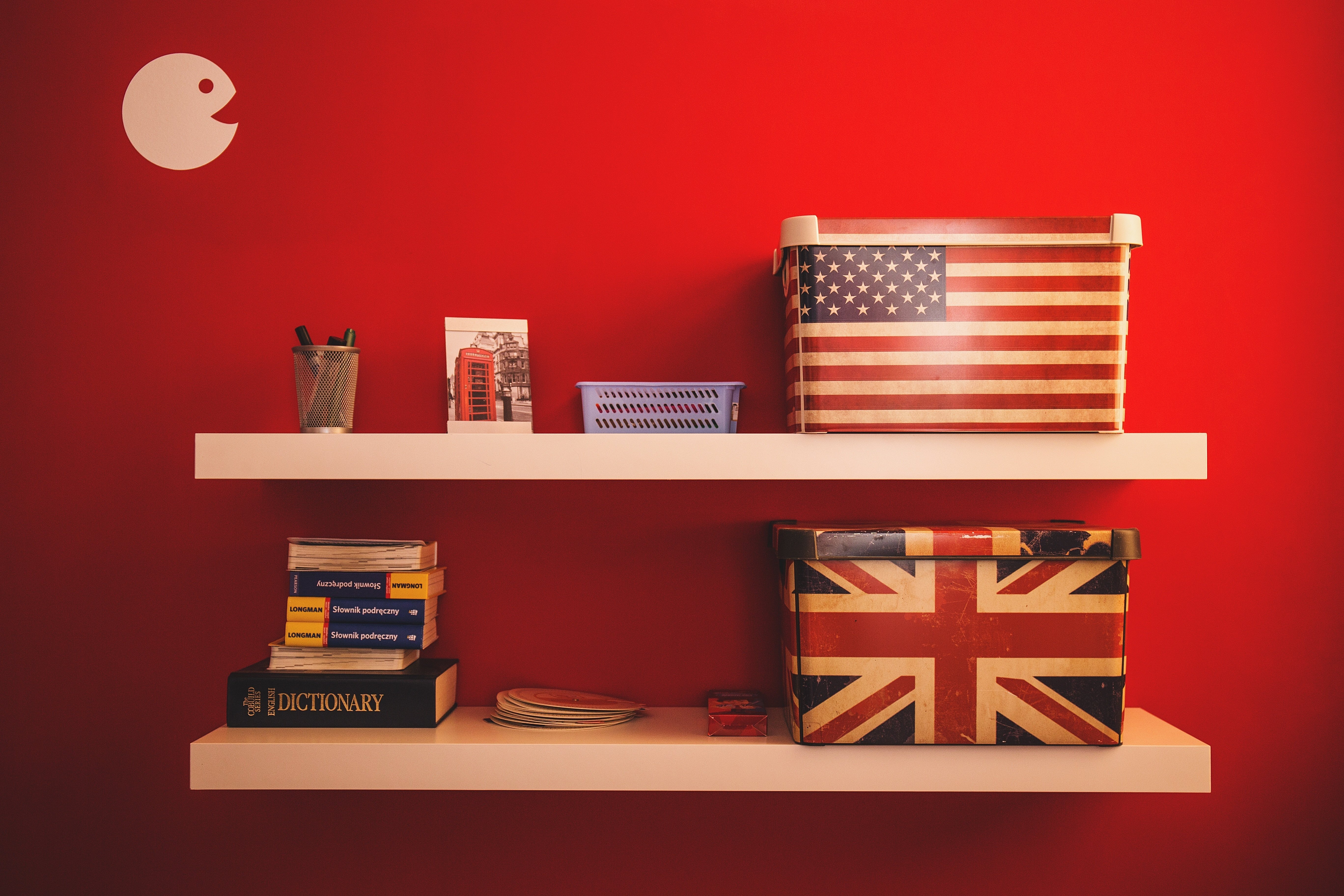 Two shelves with British and American dictionaries and flags, on a red background.