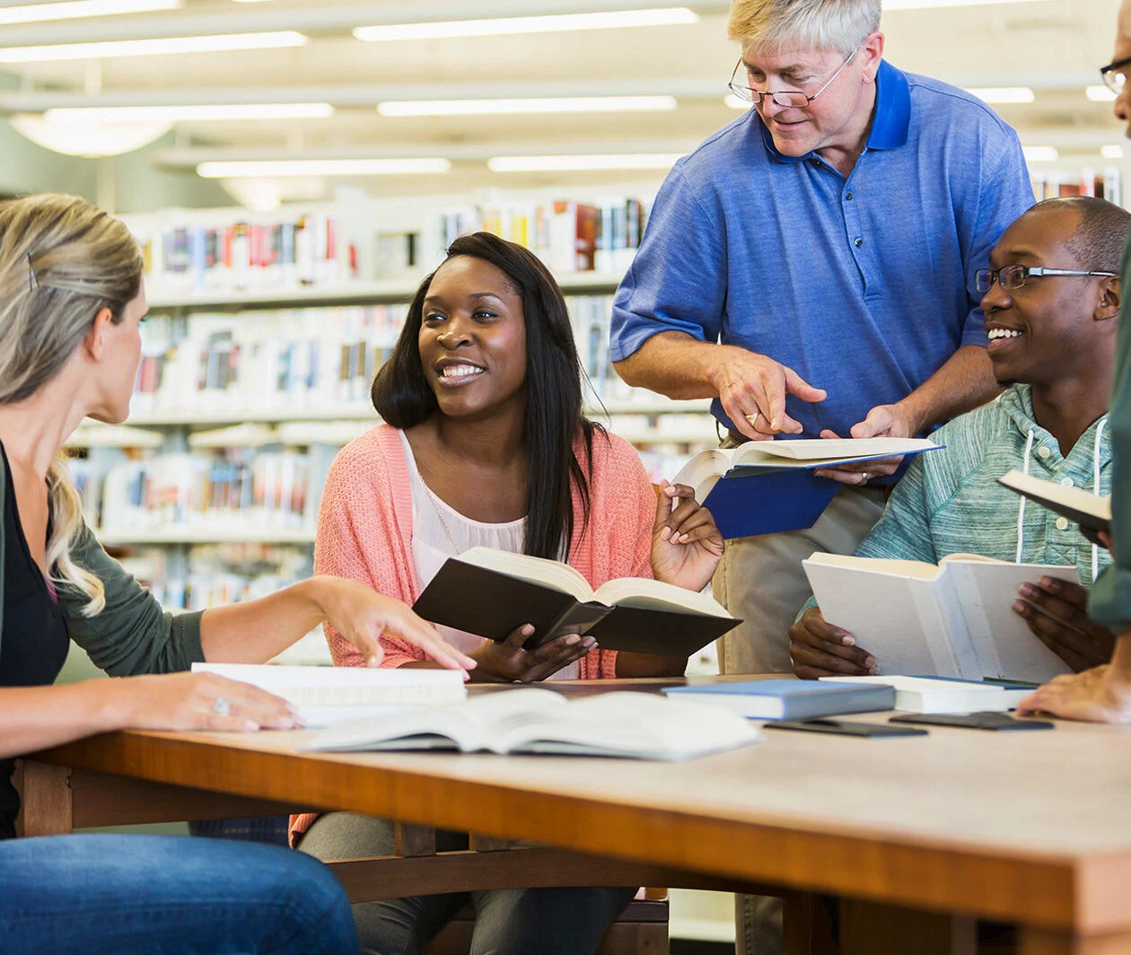 A group of people sit and read together round a wooden table in a library.